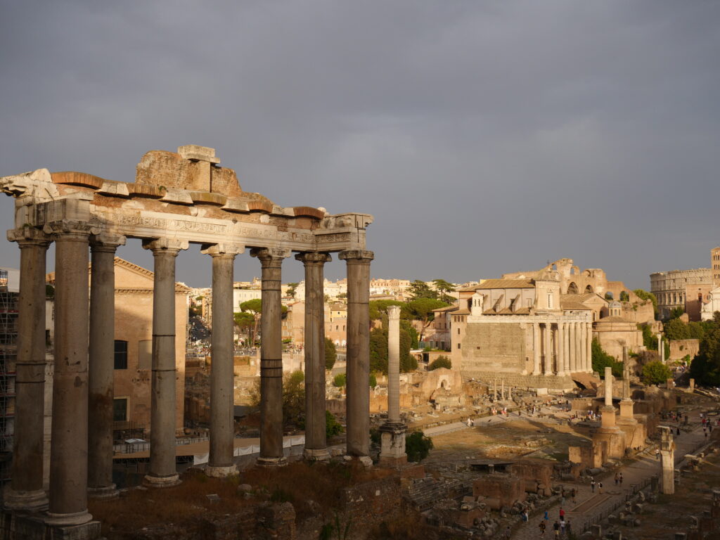 Auf einer Reise nach Rom darf ein Besuch des Foro Romano natürlich nicht fehlen. Hier auf dem Bild siehst du die Ruinen des Foro Romano, wenn die Sonne die Ruinen erstrahlen lässt, obwohl sich im Hintergrund schon die Gewitterwolken zusammenbrauen.