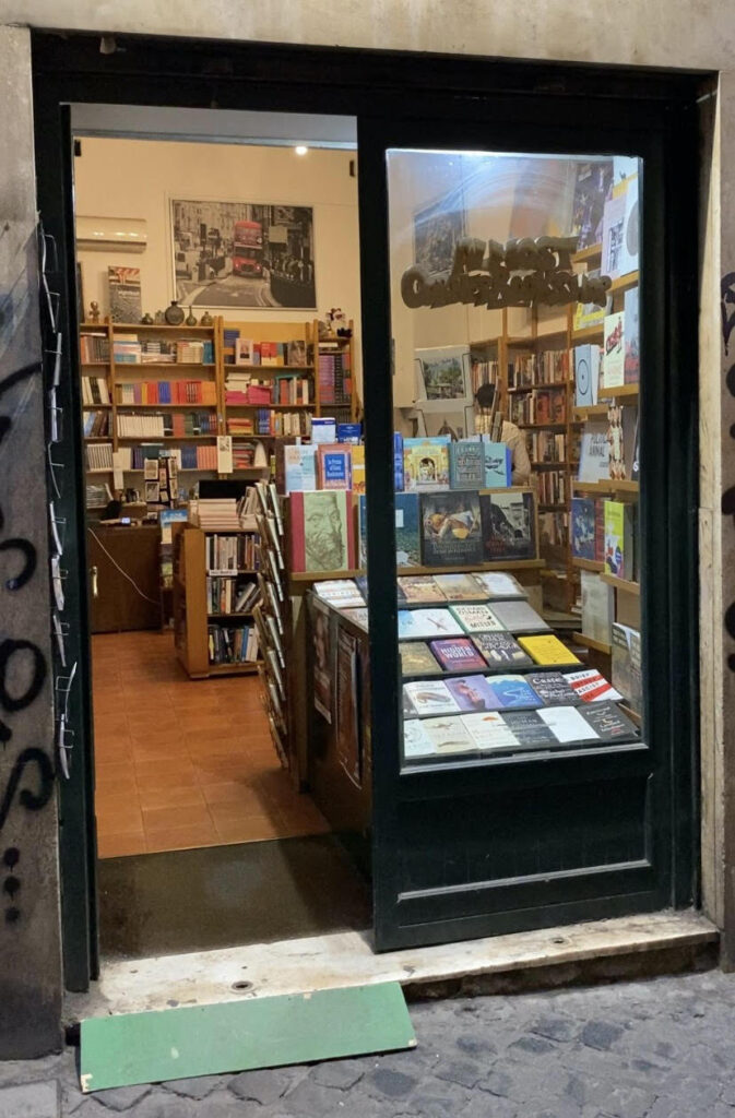 Der Eingang zum Almost Corner Bookshop ist hier mit seiner grünen Fassade zu sehen und eine große Auswahl an Büchern, die am Fenster zu sehen ist, lädt zum Reinkommen ein.