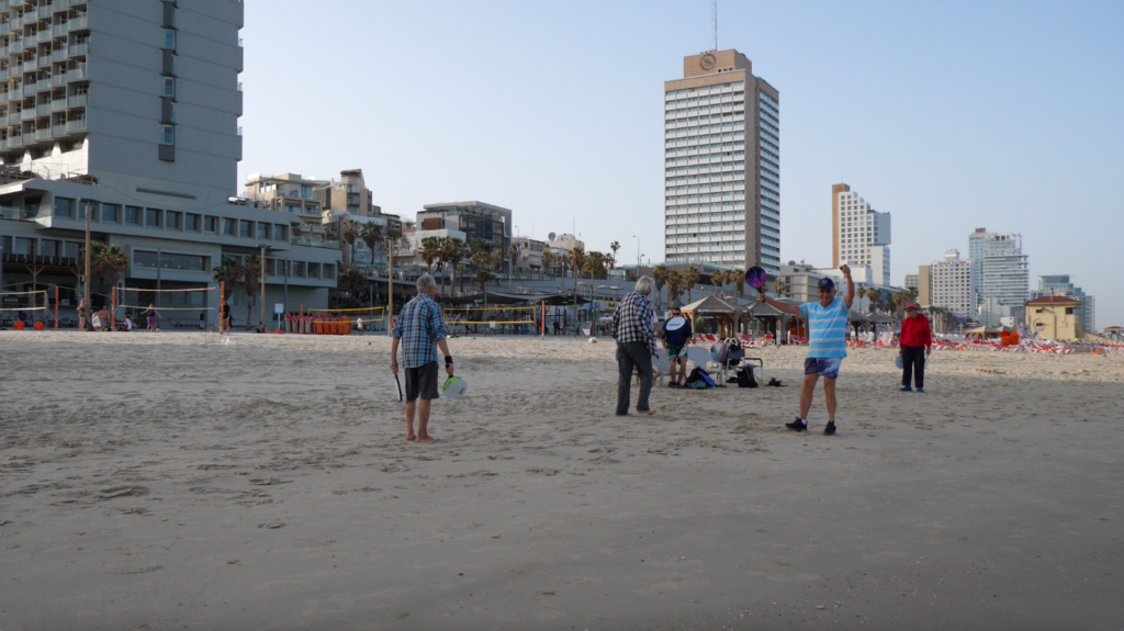 Ein Urlaub in Tel Aviv bedeutet vor allem auch zum Strand zu gehen und das Leben zu genießen. Die älteren Herren, die hier am Strand Matcott spielen, machen es vor. Im Hintergrund ist natürlich die Skyline von Tel Aviv zu sehen.